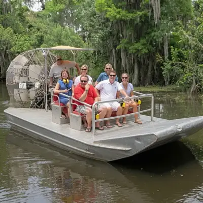 Small group of passengers on an airboat gliding past cypress trees in the Louisiana swamp