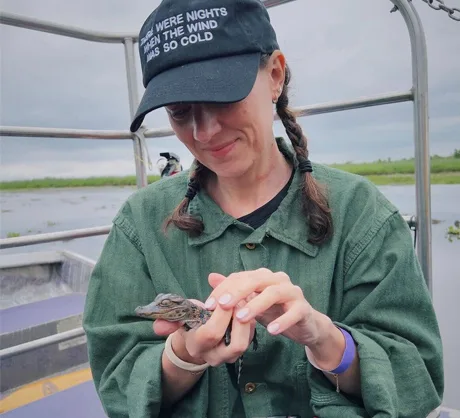 Smiling guest gently holding a baby alligator during a New Orleans swamp tour