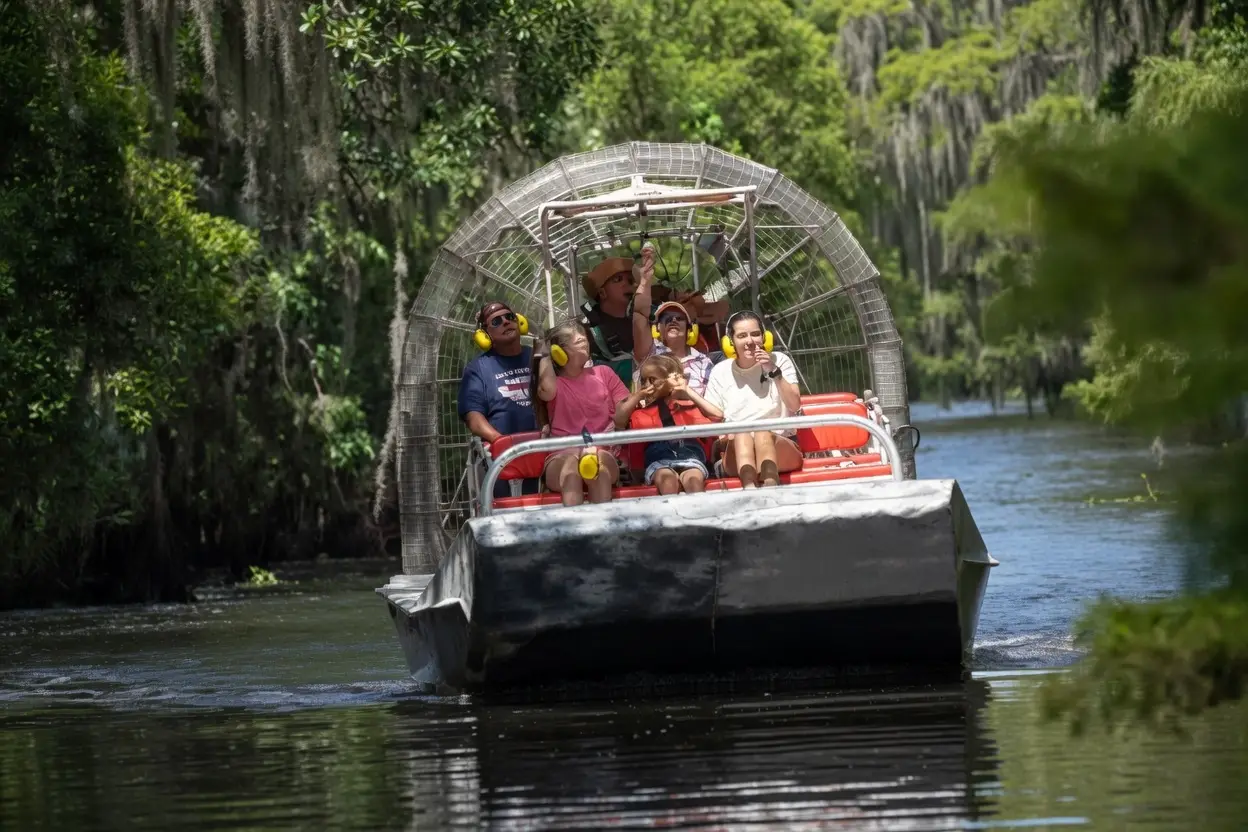 Family wearing ear protection riding an airboat through a moss-draped Louisiana bayou on a New Orleans swamp tour